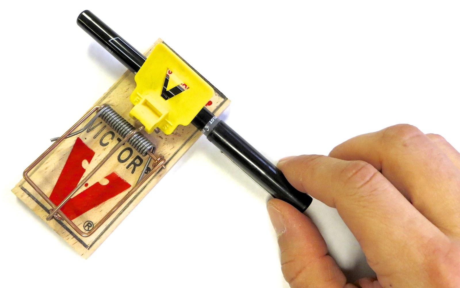 Main armant une tapette en bois à l'aide d'un stylo glissé sous la palette jaune