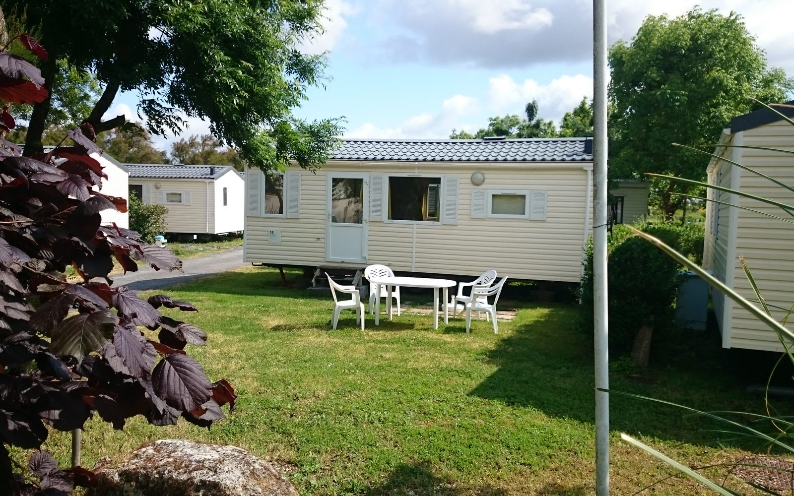 Mobil-homes blancs sur des emplacements engazonnés d'un camping, avec table et chaises de jardin devant l'un d'eux